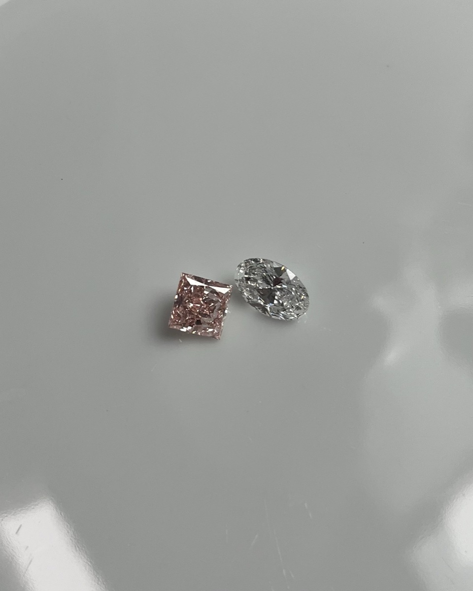 Two loose diamonds side by side, a champagne-pink stone and a colorless stone, illustrating diamond color grading
